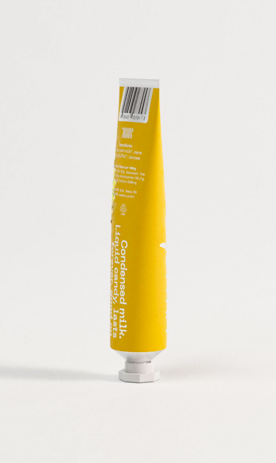 This image displays the side view of a yellow condensed milk tube, focusing on product information printed in white text. Ingredients such as whole cow’s milk, cane sugar, and lactose are listed vertically, alongside a barcode and nutritional values. The clear typographic structure supports legibility and balances regulation with design. A hexagonal white cap adds structure to the tube's form. The design reflects a branding studio’s strategy for clarity and efficiency in FMCG labeling, merging bold color with regulatory compliance.