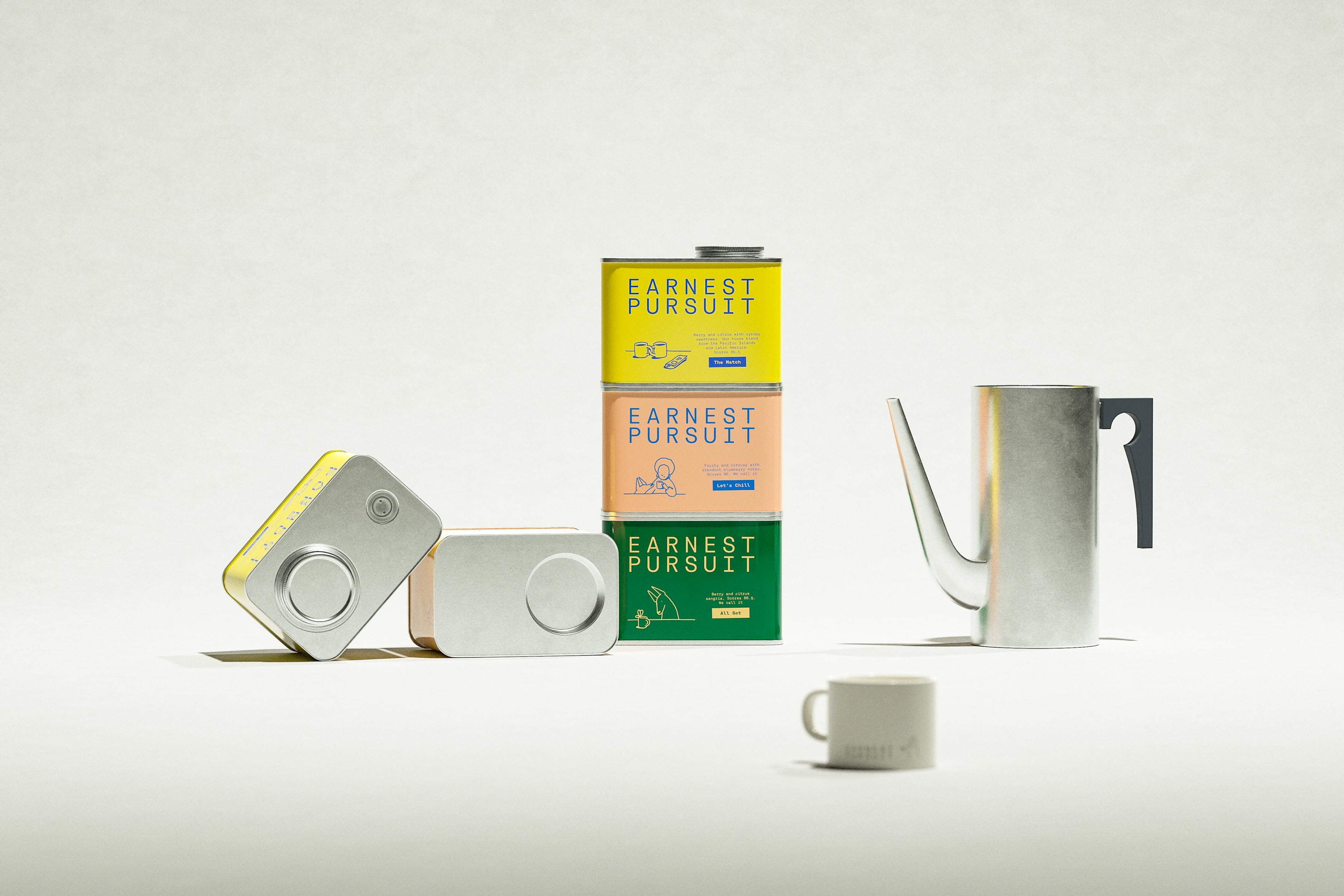 A yellow, peach and green stack stands in the middle of a pale set, flanked by two tins lying on their sides to show bare metal ends, a brushed-silver pitcher with a charcoal handle on the right and a small cream mug in the foreground. The stack is where the color lives; everything else is metal, ceramic and calm. Art direction that lets the tins be the only things with a personality, and not a single coffee bean in sight. Branding and packaging design by Art of Packaging, which can style a coffee scene without any coffee.