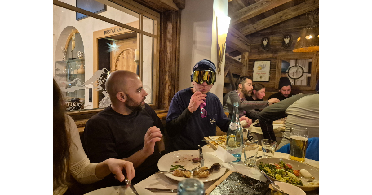 Team members sitting around tables in an alpine lodge, sharing a meal.