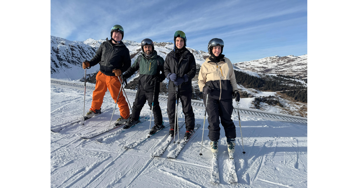 Anchor teammates atop a snowy ski slope, alpine mountains in the background. 