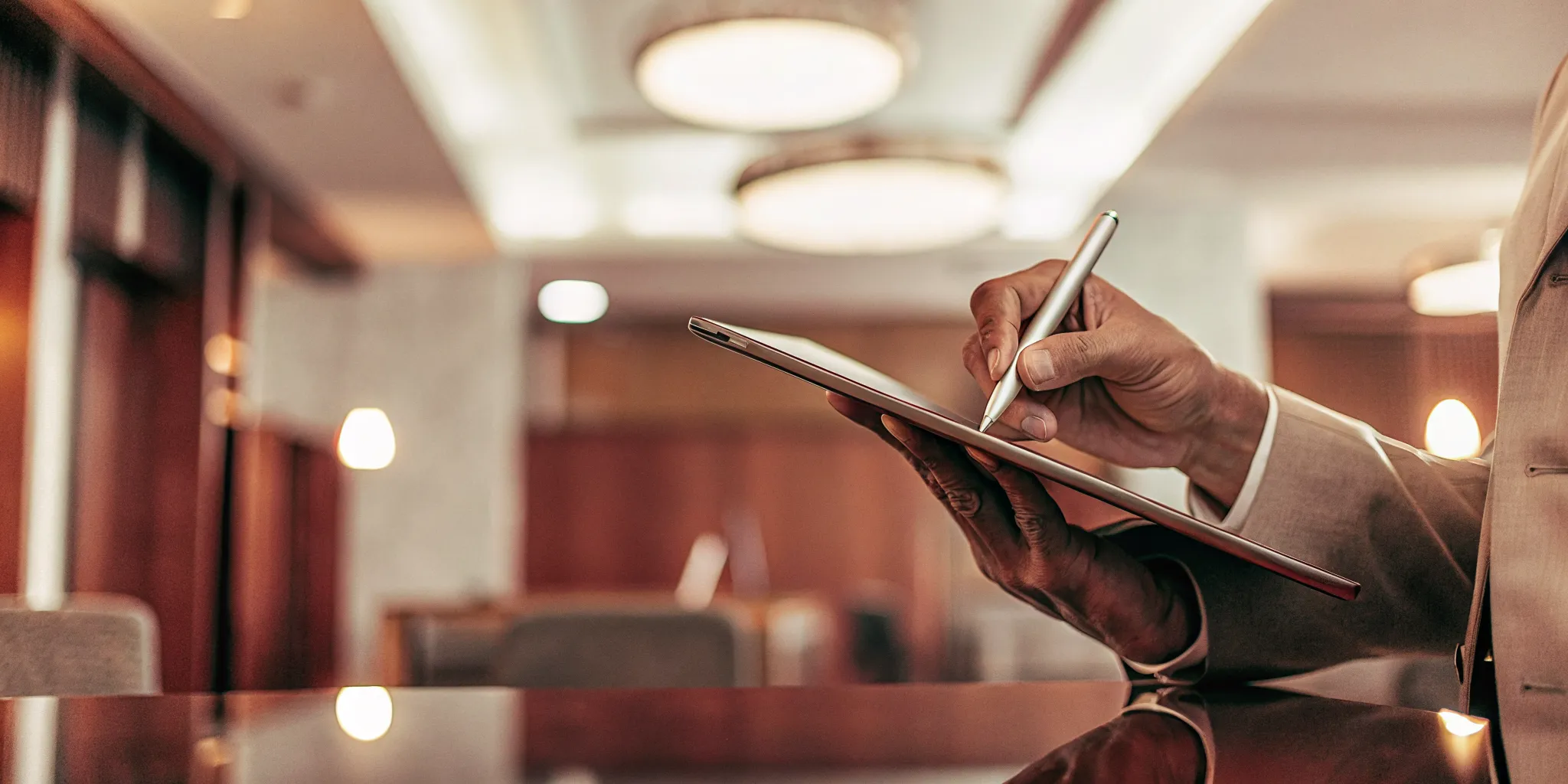 A close up of a hand signing a digital proposal on a tablet in a modern professional office setting