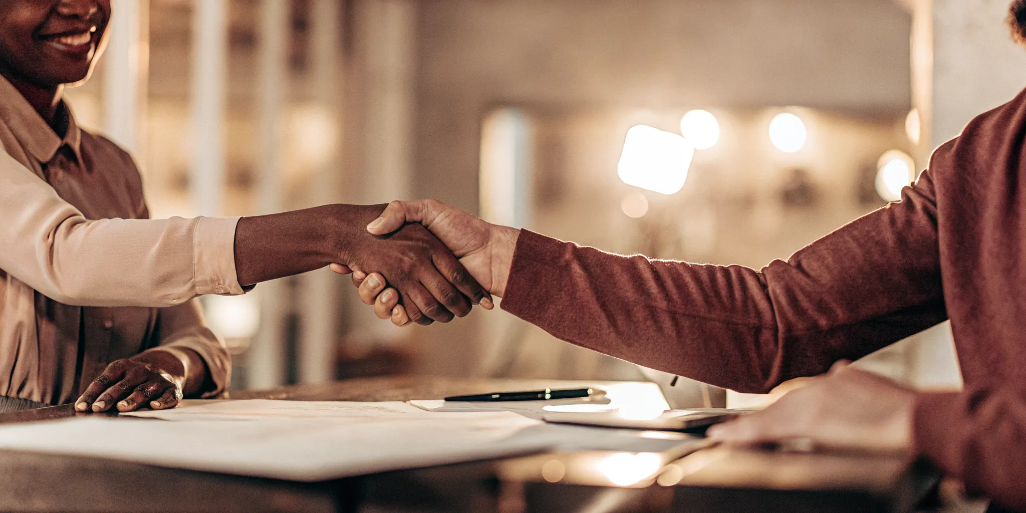 Bookkeeper and client shaking hands over a signed agreement in a bright modern office