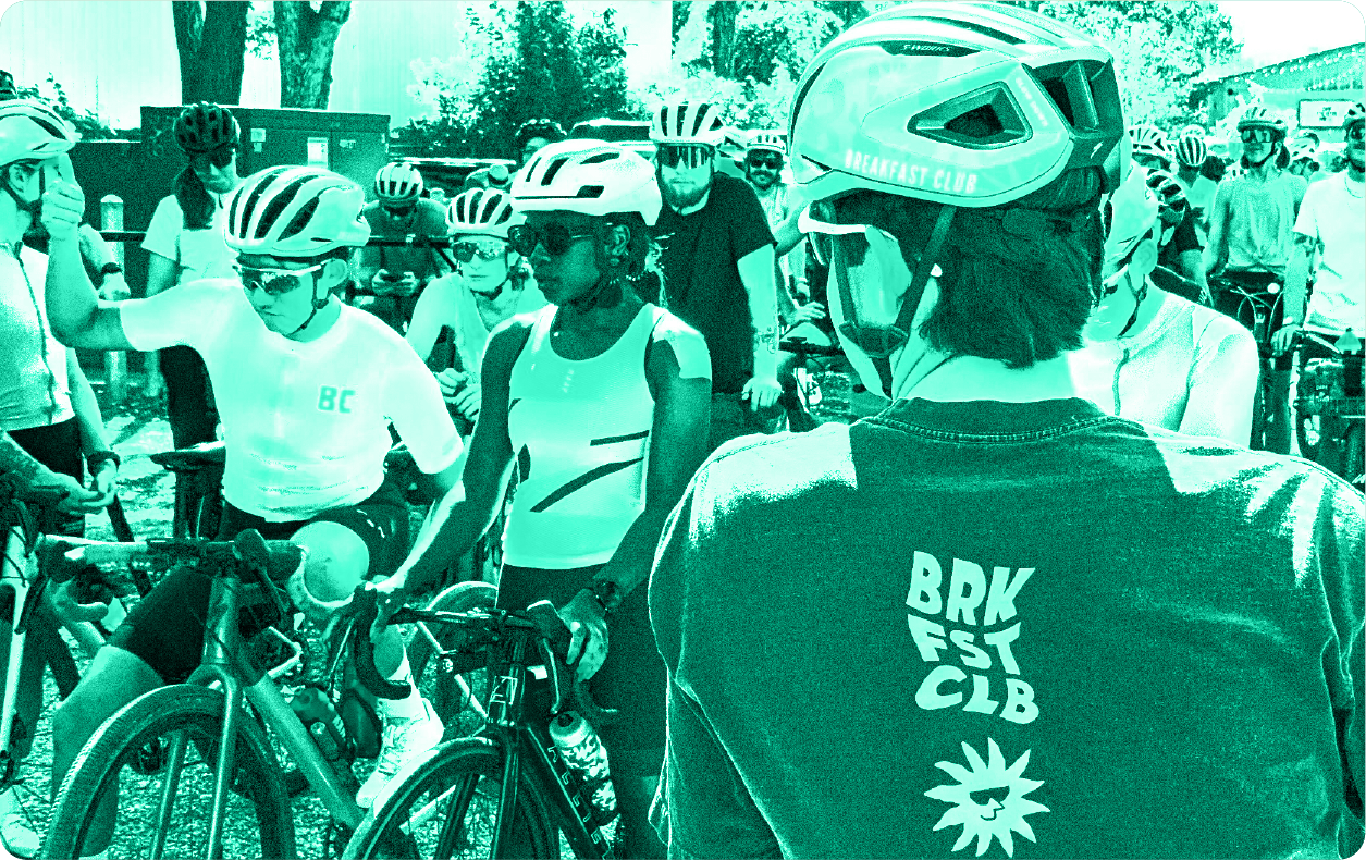 Cyclists wearing helmets and sunglasses gathered with their bikes in an outdoor setting on a sunny day.