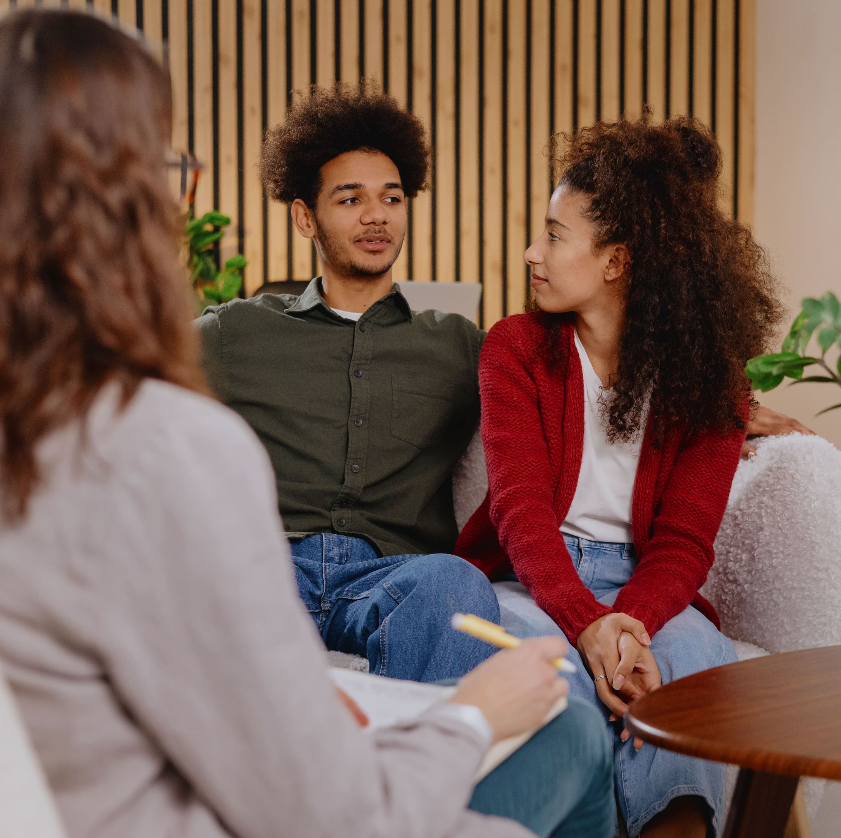 A couple seated on a couch talking to a therapist who is taking notes.