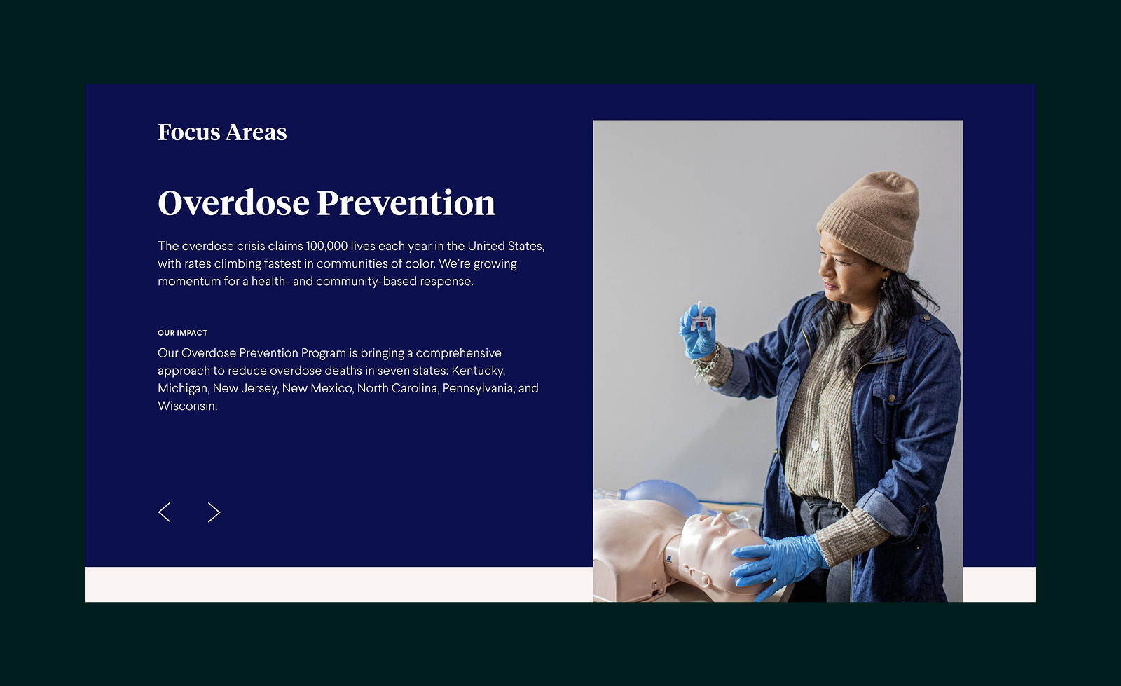 Person wearing blue gloves and a beige beanie holds a small container over a CPR training mannequin in a demonstration setting.
