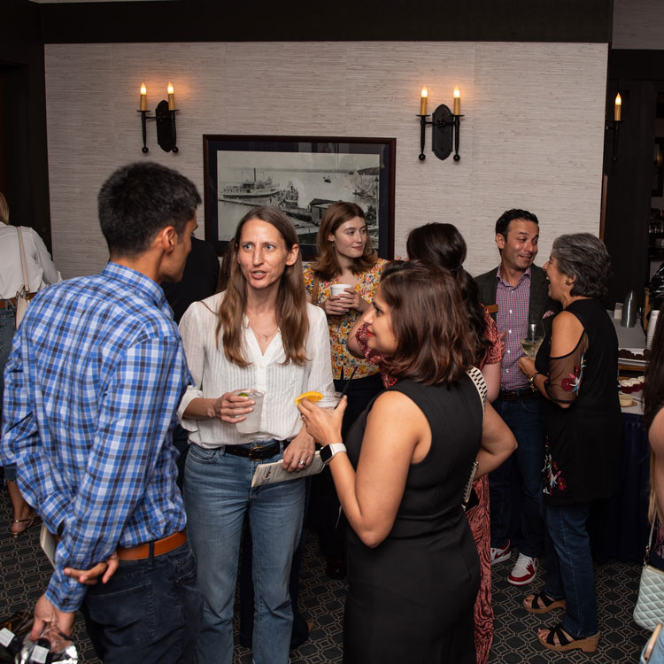 Group of people socializing indoors at a casual event, holding drinks and engaging in conversation.