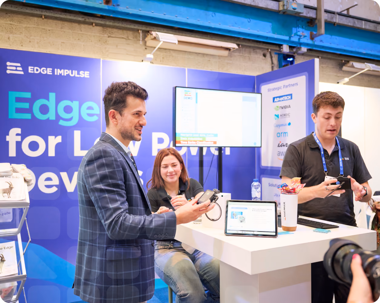 Edge Impulse team demonstrating AI tools at an event booth, with exclusive swag and tech gear displayed for ambassadors.