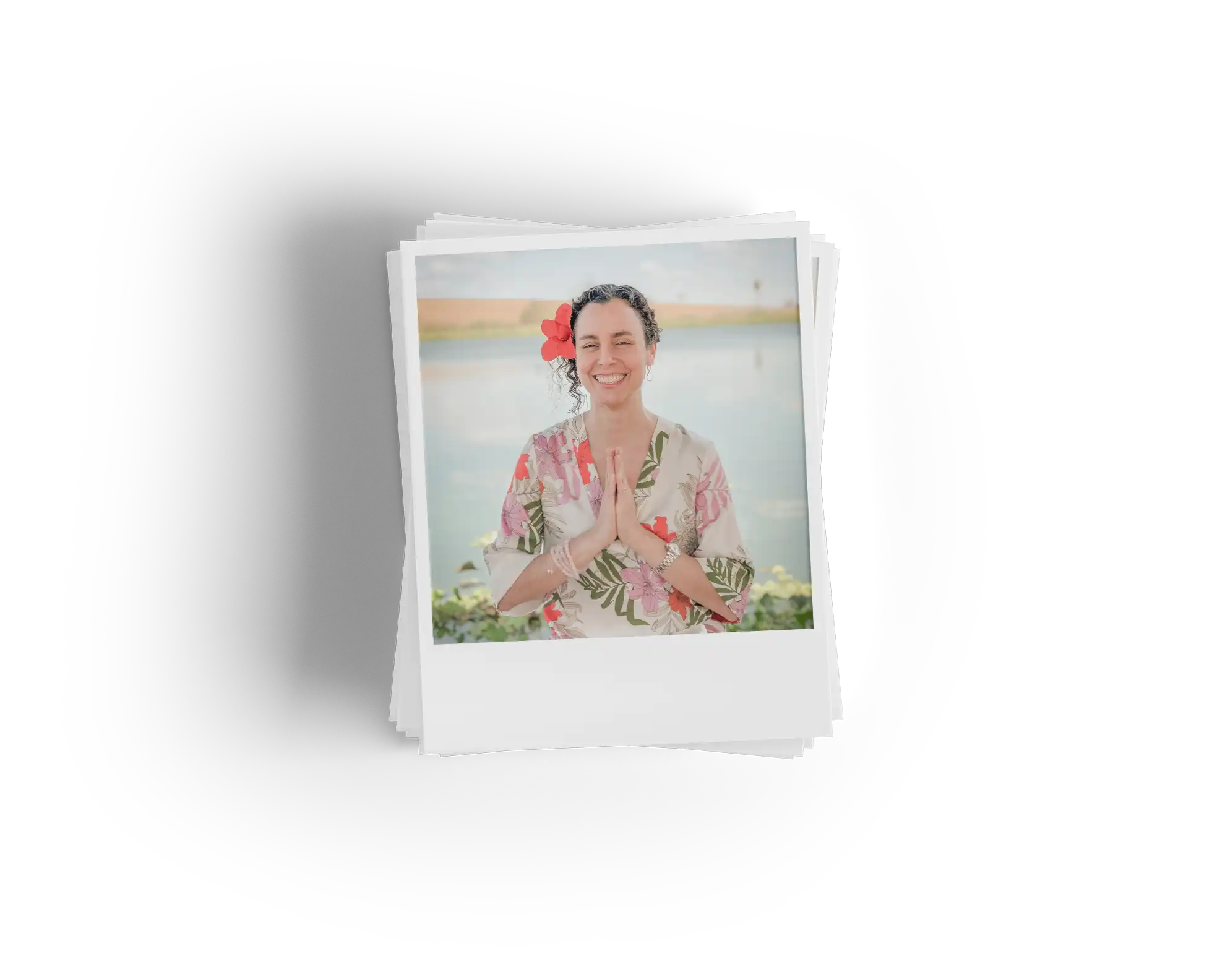 Foto estilo Polaroid de Thaís Ghussn, fundadora da agência Thaís Tours, sorrindo com as mãos juntas em gesto de agradecimento, usando uma flor vermelha no cabelo e roupa florida com estampa de folhas.