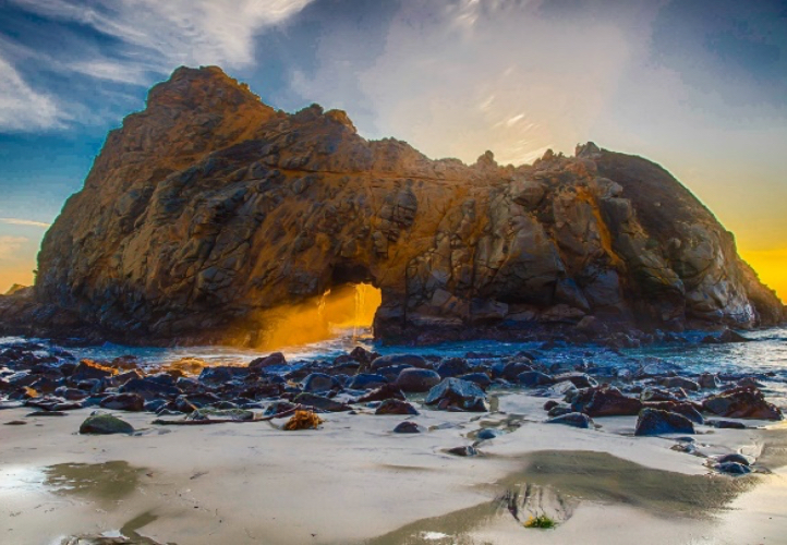 A rock formation with an opening in the middle of it where sun is shining through.
