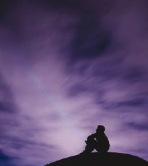 A person sitting on hill gazing up at darkening sky.