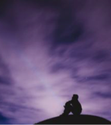 A person sits and looks up at the night sky from a hilltop.