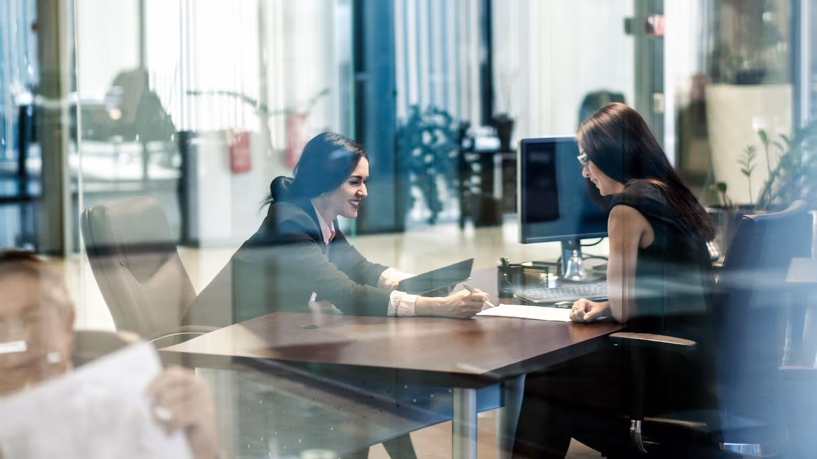 A person sitting at a table with another person in the backgroundAI-generated content may be incorrect.
