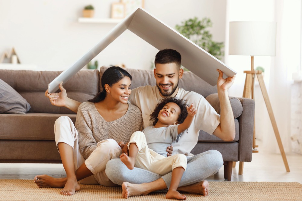 Happy family sitting on the floor under a roof-shaped cover at home.