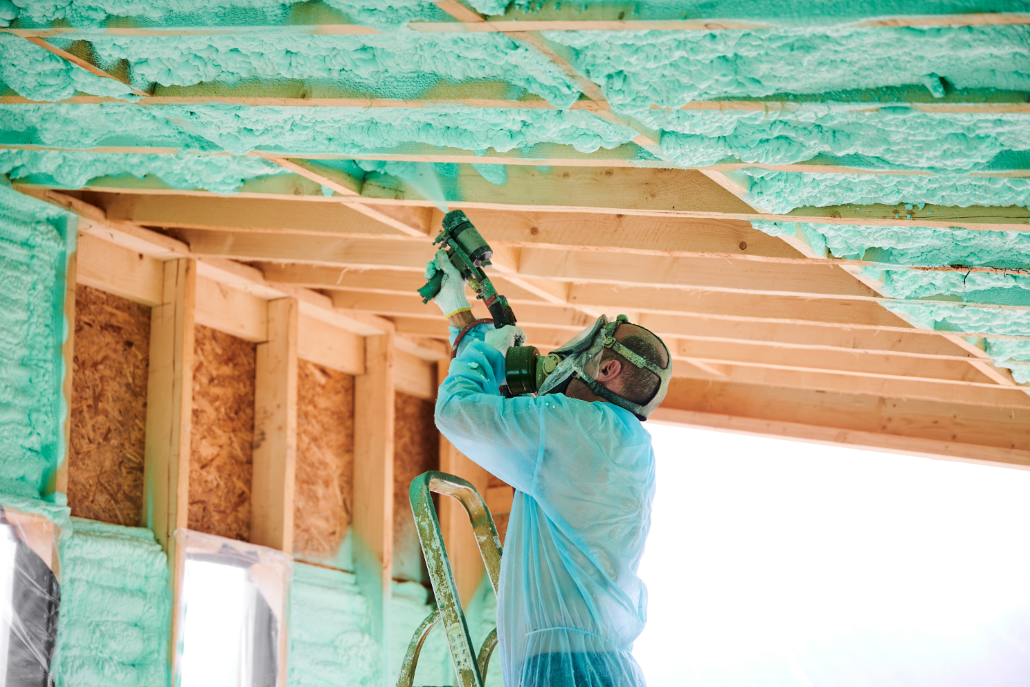 Worker sprays insulation foam on ceiling beams.