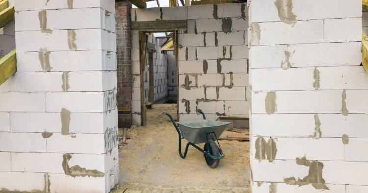 Unfinished building with grey cinder blocks and a wheelbarrow.