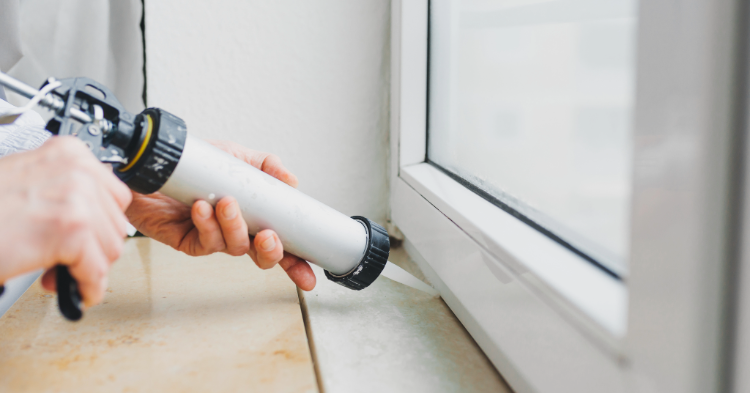 Person sealing window with caulk gun.
