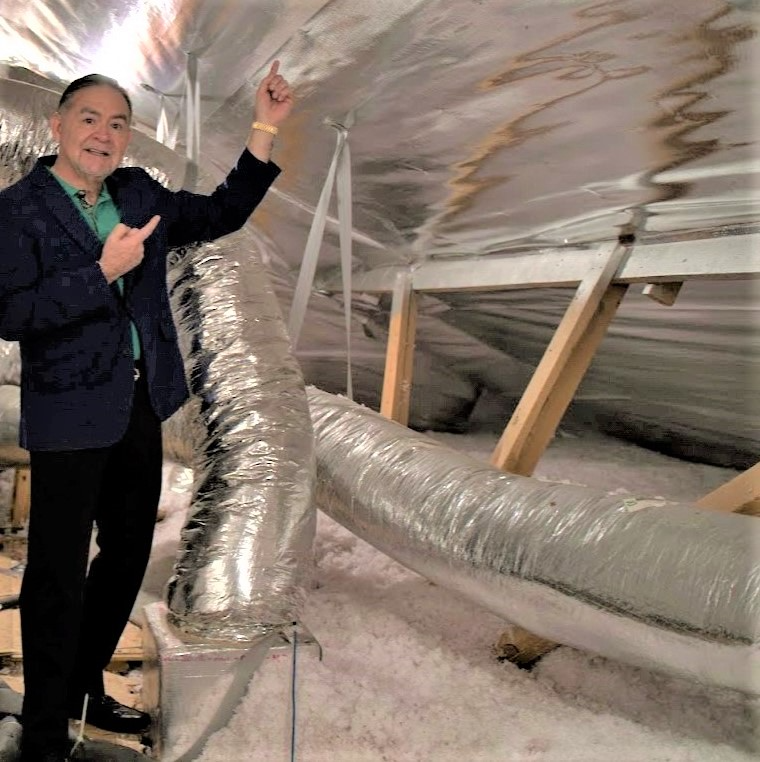 Richard Ramos standing in an attic with radiant barrier insulation, gesturing toward the insulation around him