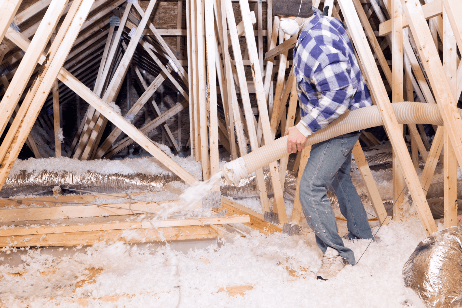 Worker blowing R-30 blown-in fiberglass insulation into an attic using a large hose