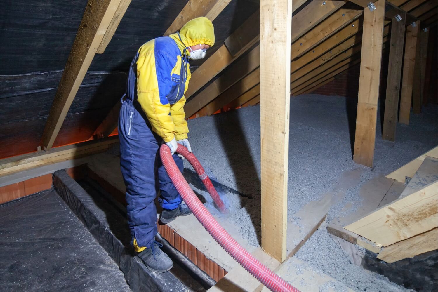 Contractor in protective gear installing blown-in attic insulation rated R-30 to improve energy efficiency and lower heating and cooling costs.