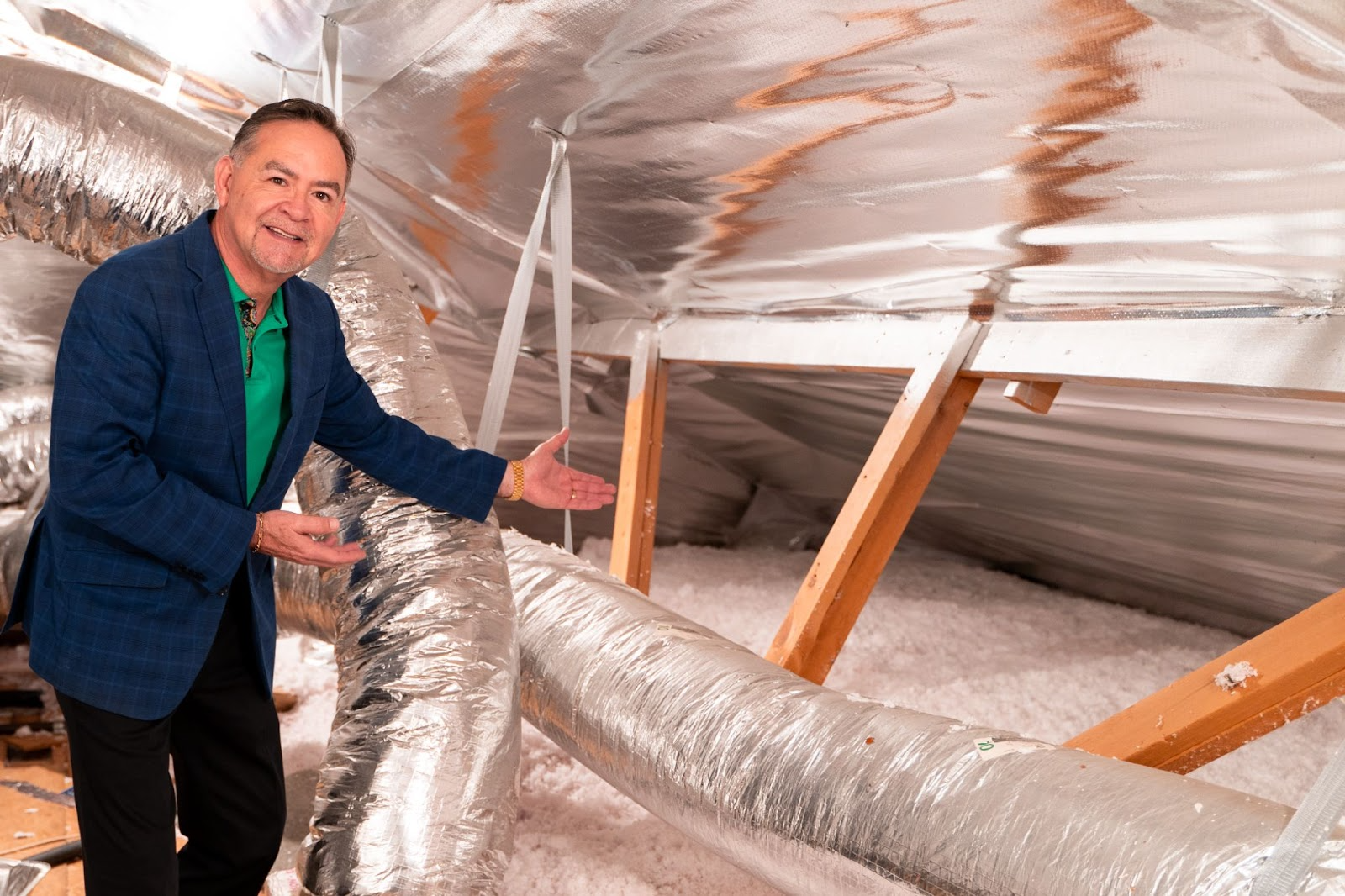 Richard Ramos standing in an attic with radiant barrier insulation, gesturing toward the ductwork and insulation around him