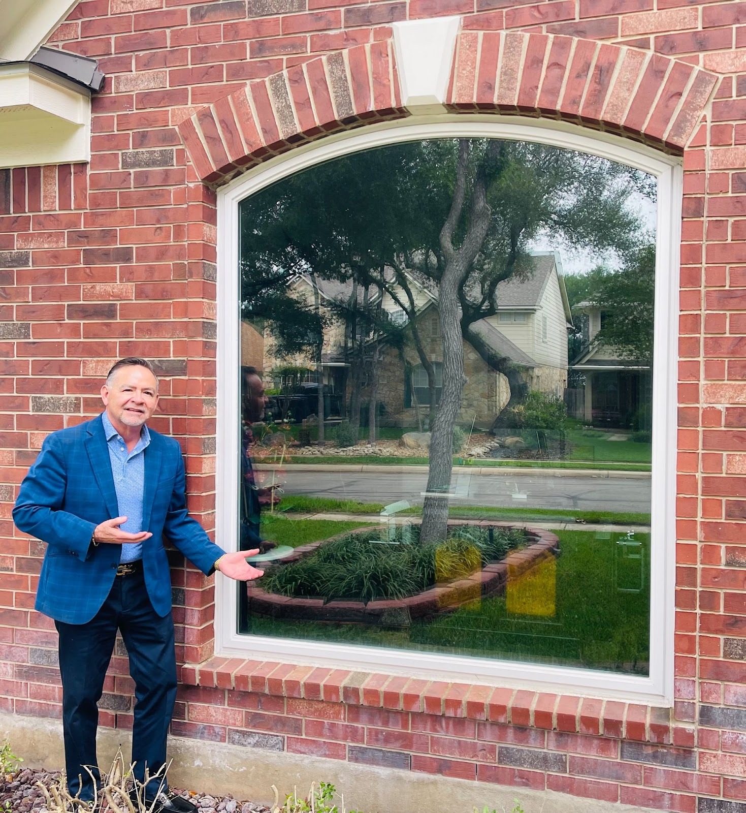 Richard Ramos from Green Energy of San Antonio standing outside a brick house beside a large arched window, gesturing toward it with both hands.