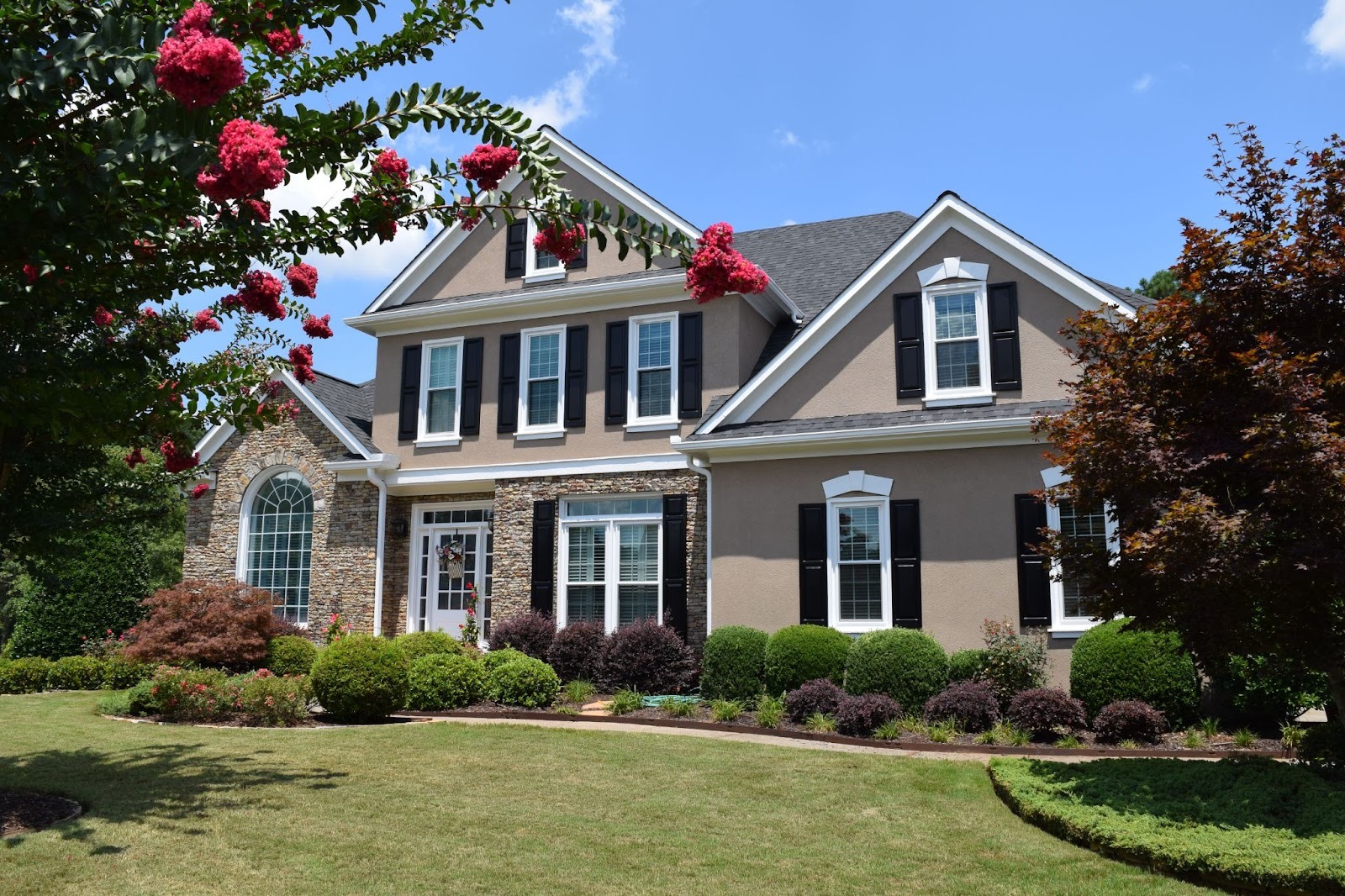 Modern two-story suburban house with white windows, black shutters, stone accents, and landscaped front yard