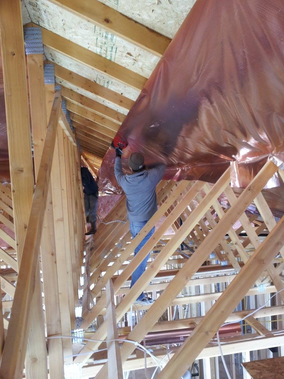 Workers installing reflective radiant barrier insulation between wooden roof trusses.