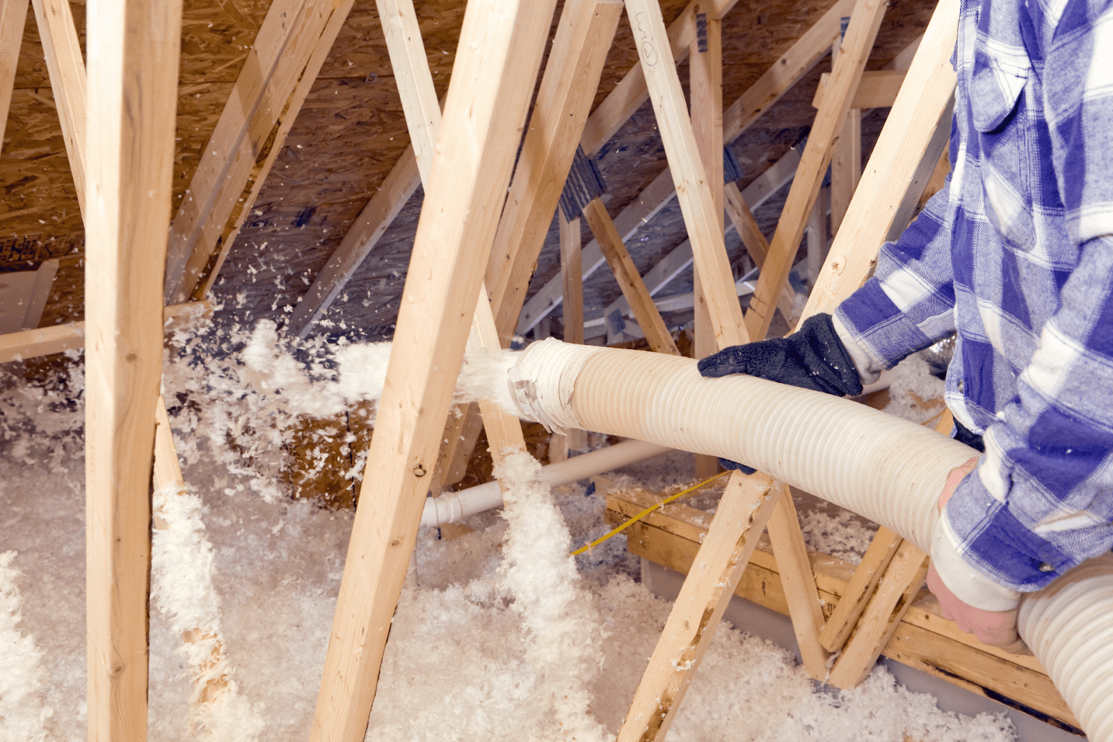 Worker Spraying Blown Fiberglass Insulation between Attic Trusses