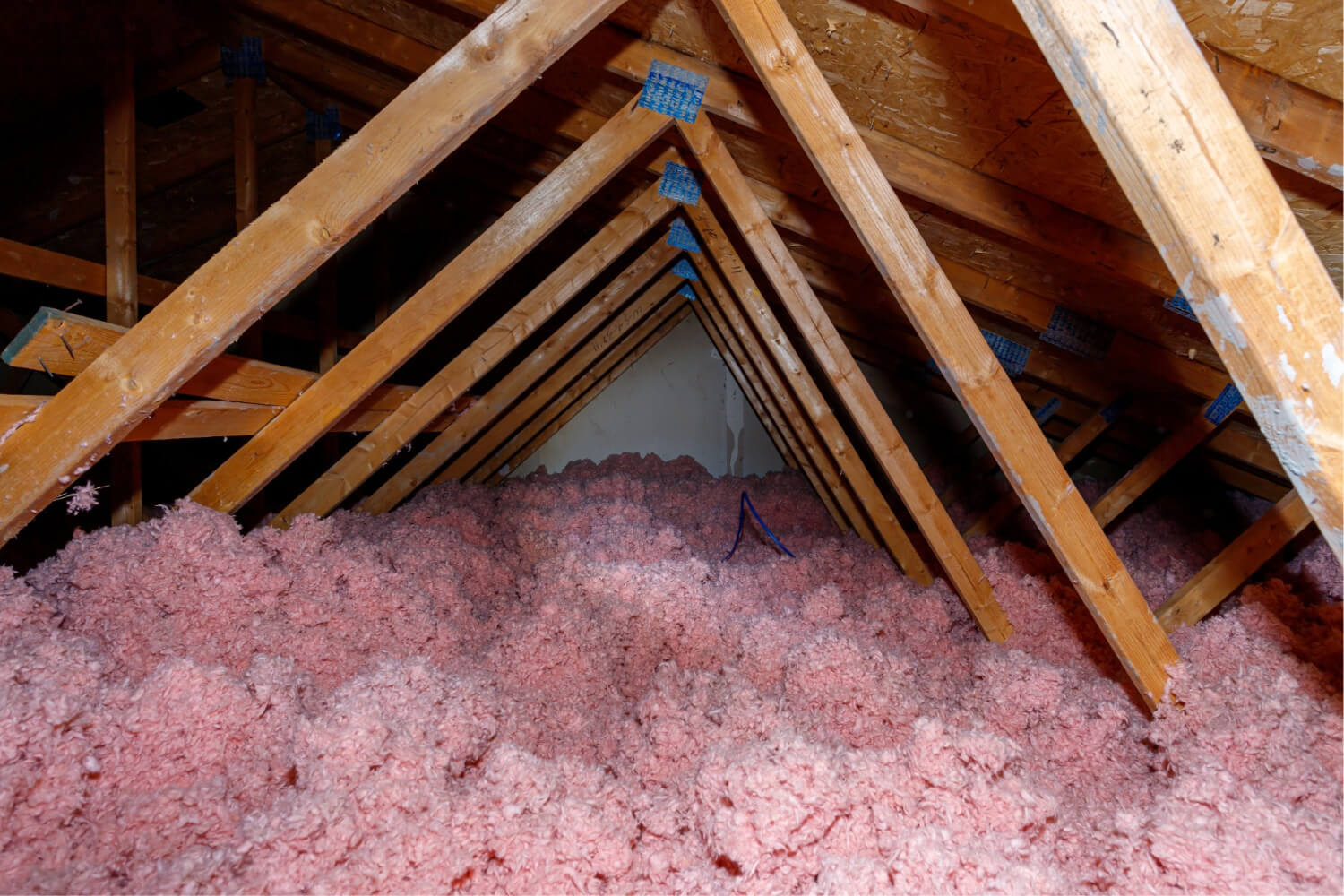 Attic space with exposed wooden beams and pink insulation.