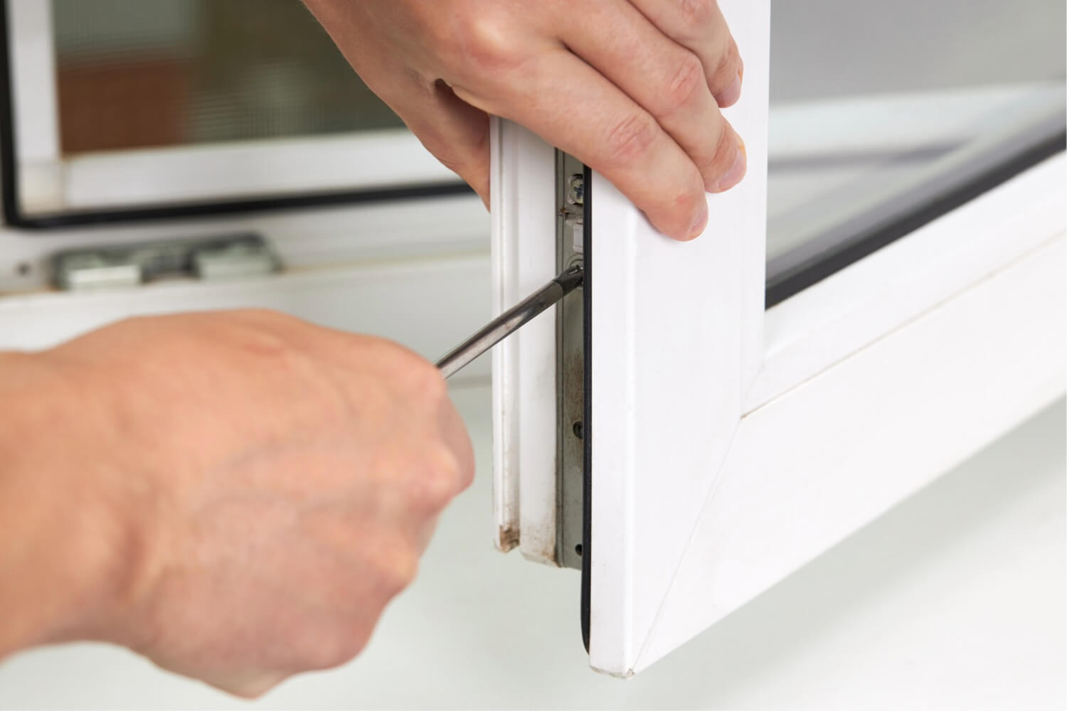 Hands tightening a window hinge with a screwdriver.