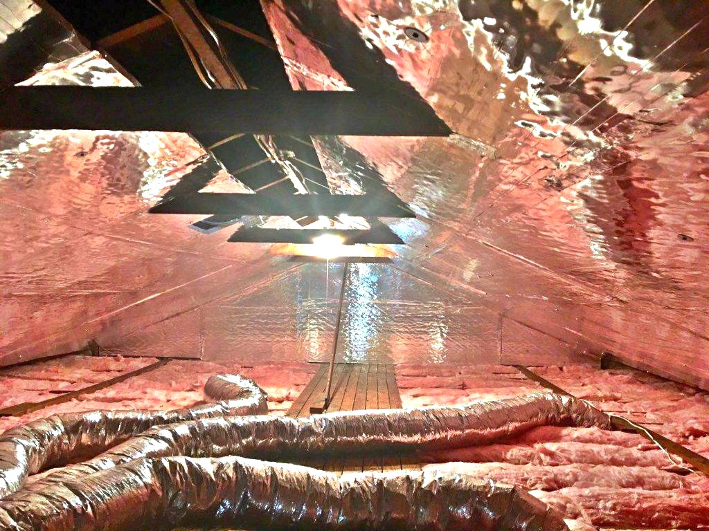 Attic lined with reflective radiant barrier insulation and air ducts running across the floor