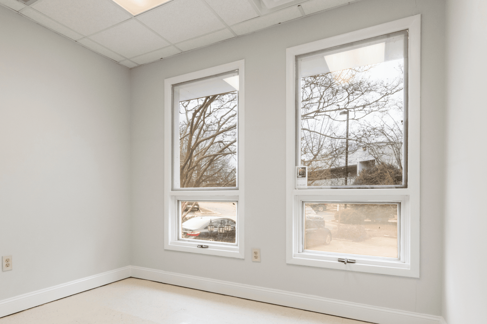 Interior view of a room with two single-hung windows showing a parking area and trees outside.