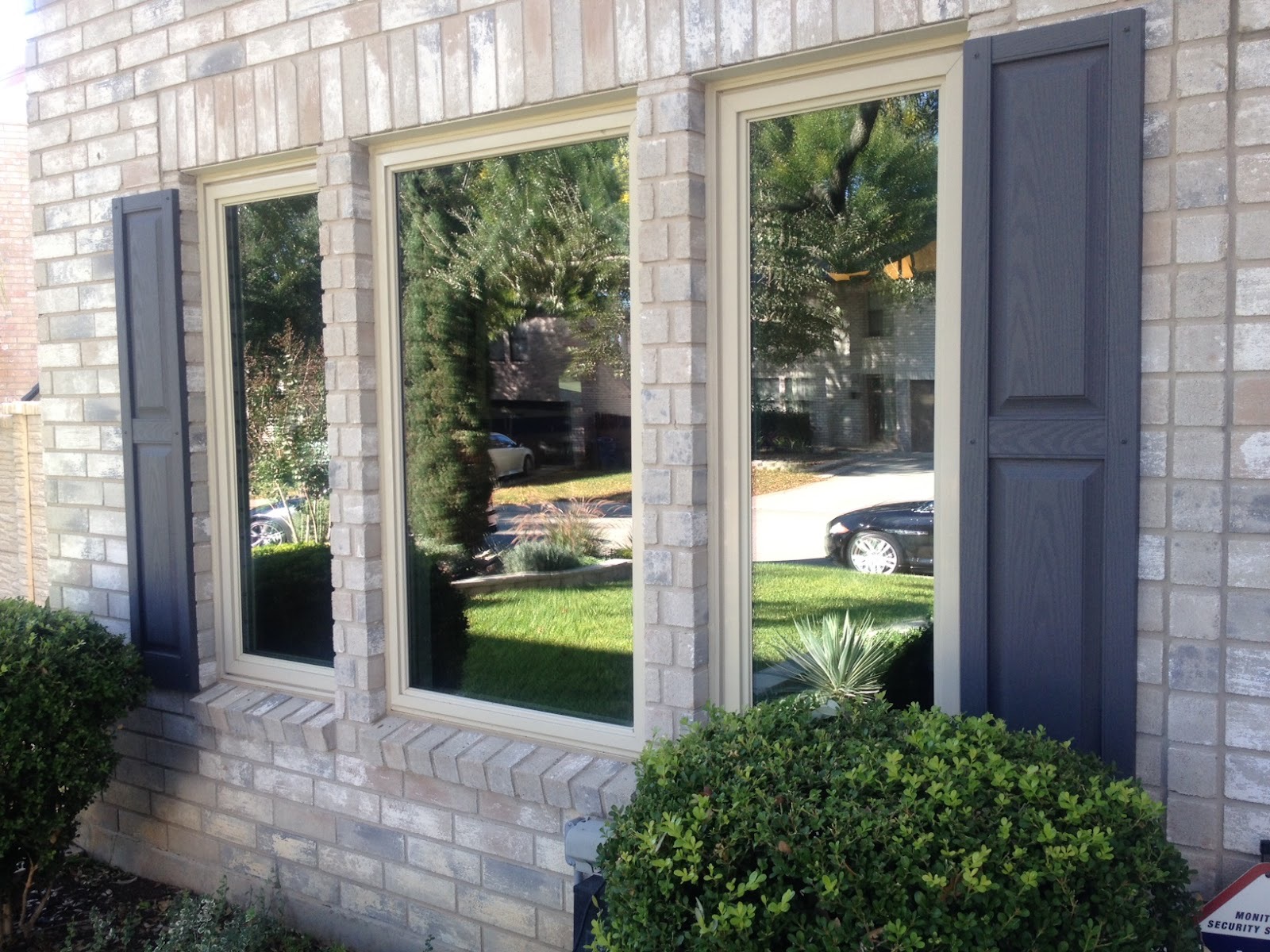 Close-up of house windows with dark shutters reflecting greenery and parked cars