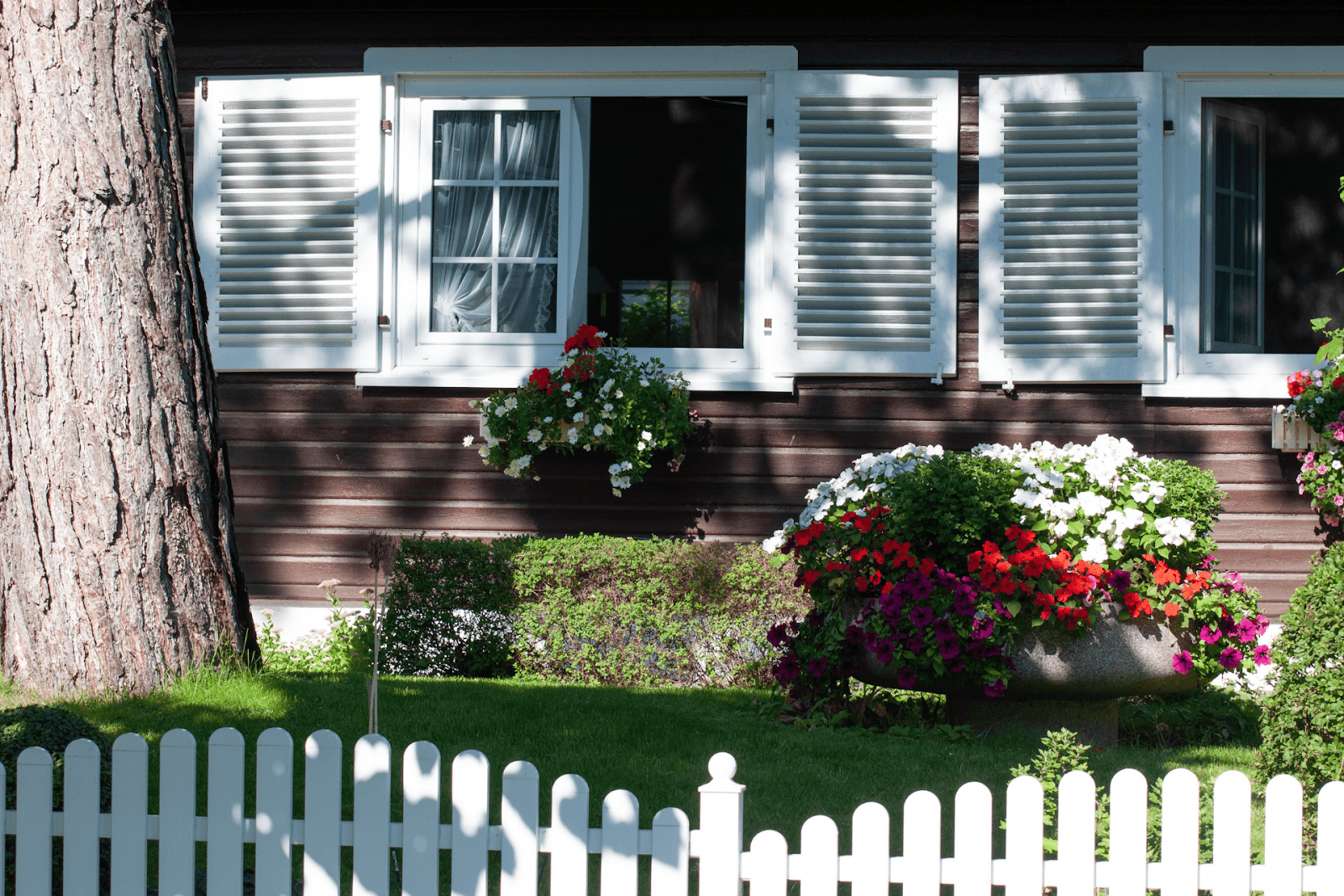 House exterior with white shutters, a picket fence, and colorful flowers in planters