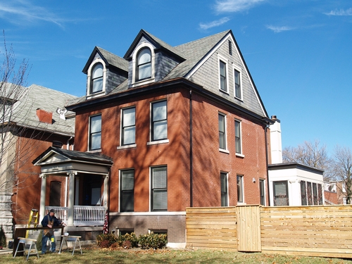A restored historic single family home. It is mostly red brick, with brown brick around the basement level and grey slats on the exterior of the top floor.