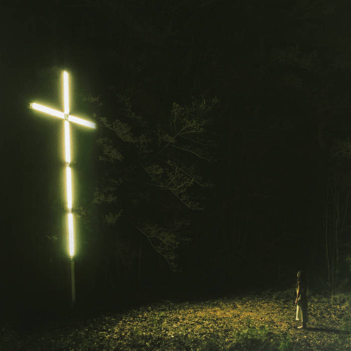 person staring at a huge neon cross in a field
