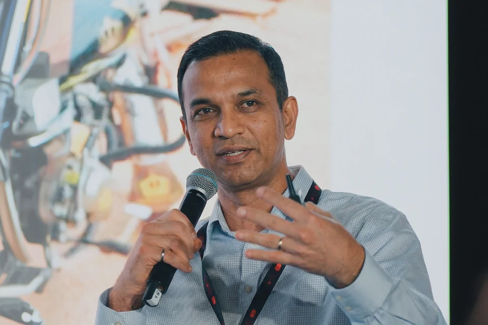 Man in a blue shirt speaking into a microphone while gesturing with his hand.