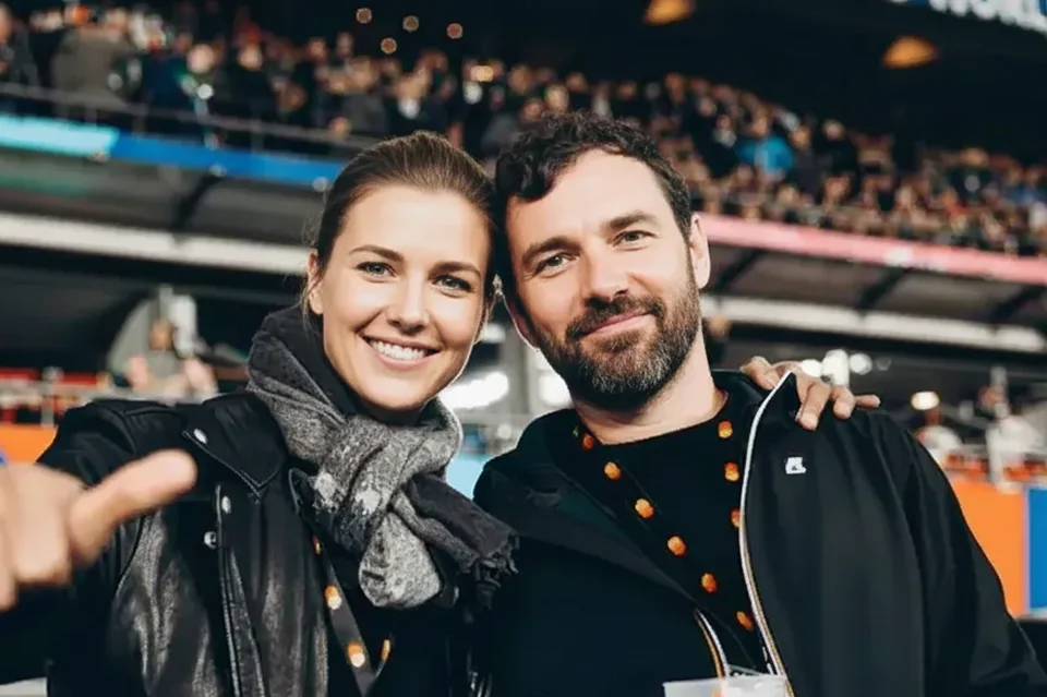 Smiling man and woman posing closely with arm around each other at a crowded event.