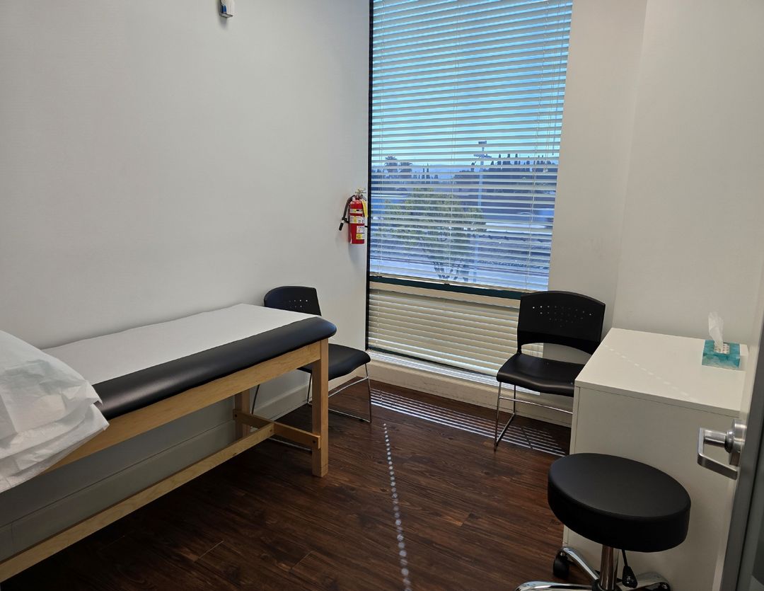 Pain management exam room with a treatment table, chairs and a window