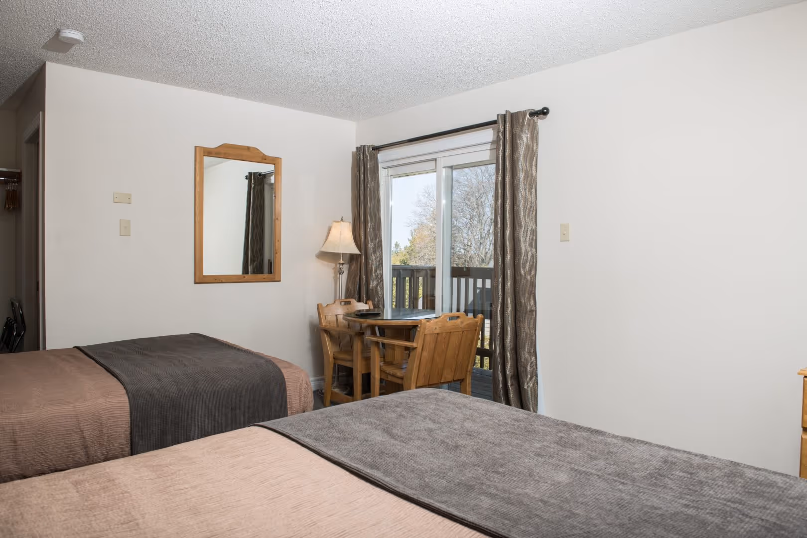 Hotel room with two beds, a small wooden table with two chairs, and glass doors leading to a balcony.