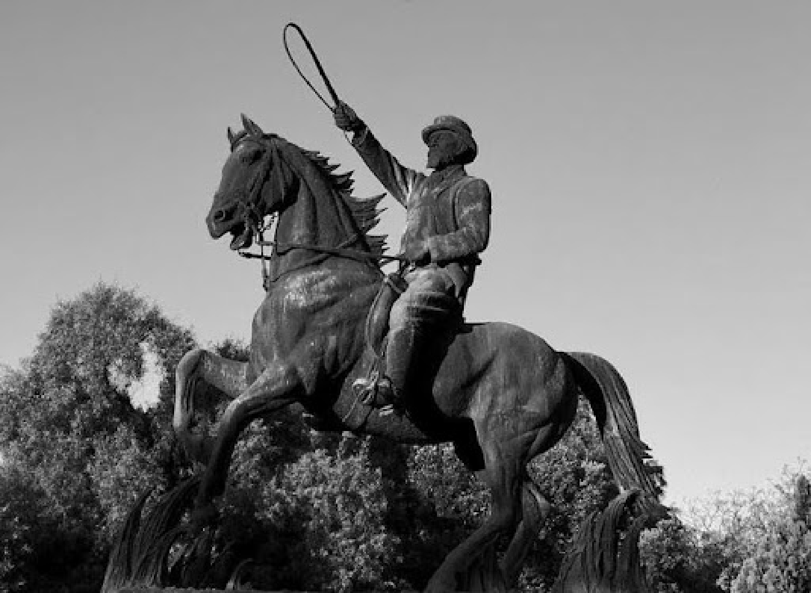 Bronze statue of a man on a rearing horse holding a whip in his raised right hand.