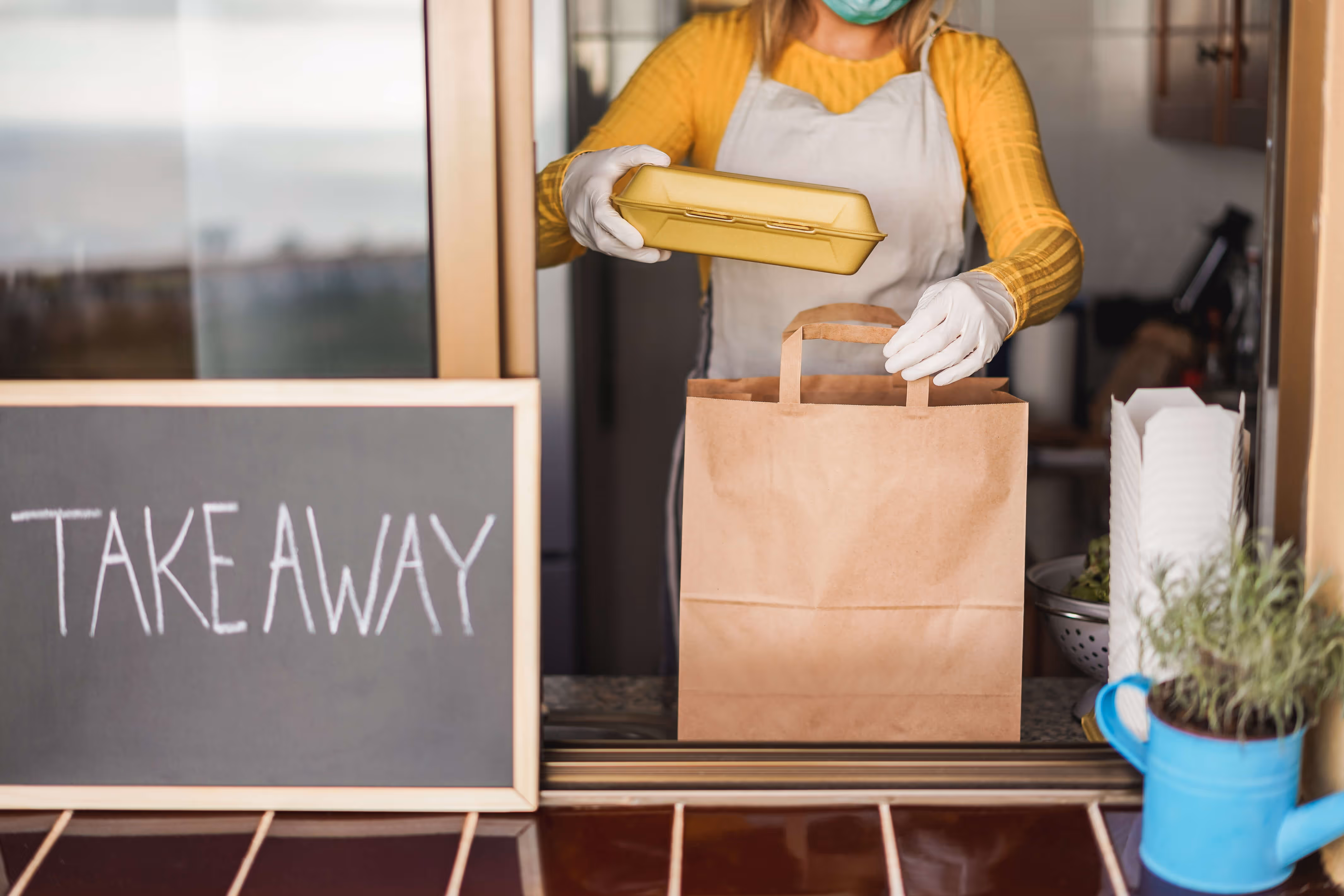 Serveuse portant un masque met un repas dans un sac en papier pour un service à emporter.