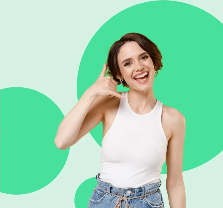Mujer sonriente con camiseta blanca y pantalones de mezclilla, haciendo un gesto de llamada con la mano, sobre fondo verde.