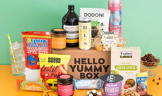 Variety of snacks and beverages arranged around a box labeled 'Hello Yummy Box' on a yellow and green background.