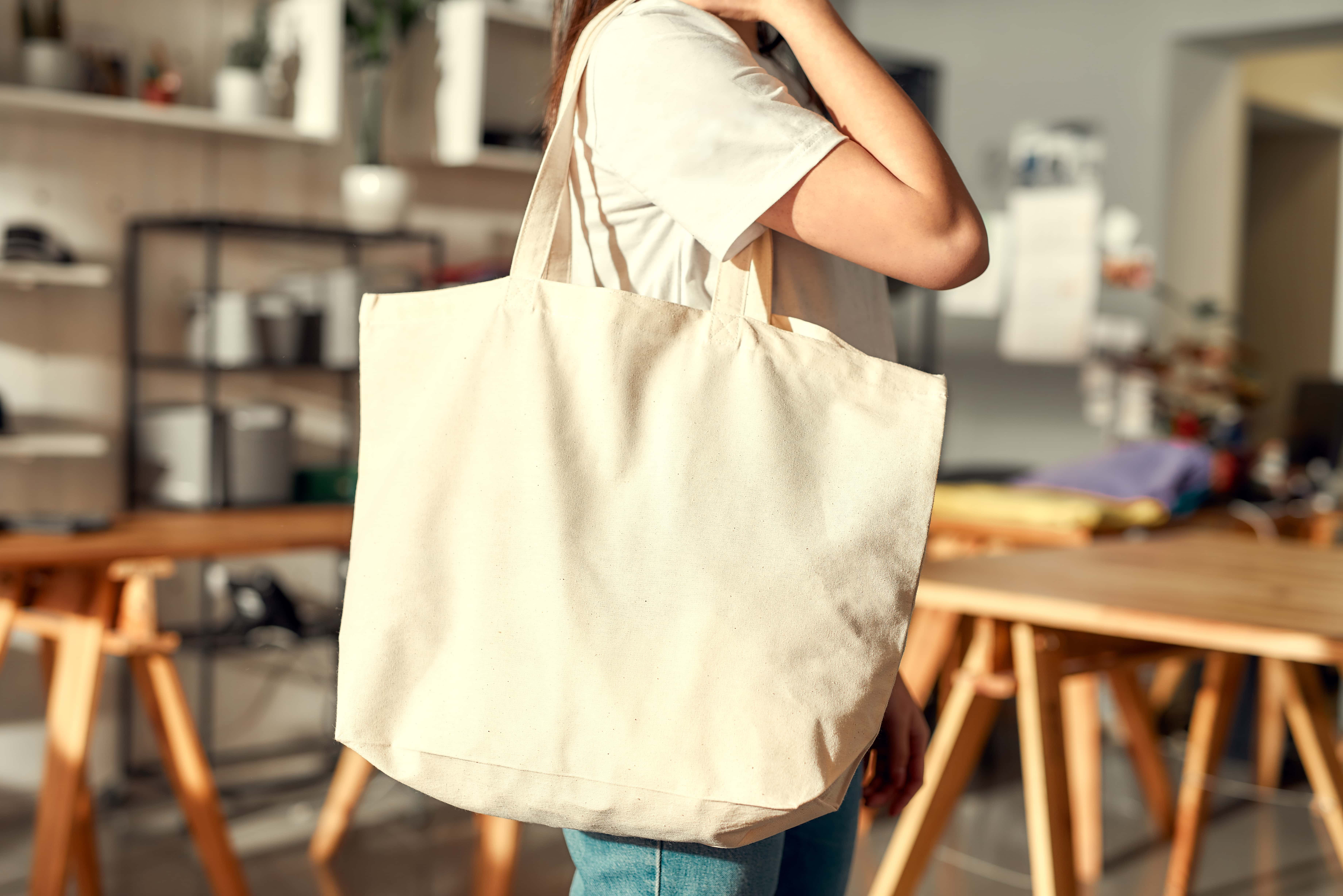 Person holding a blank canvas tote bag ready to be customized.