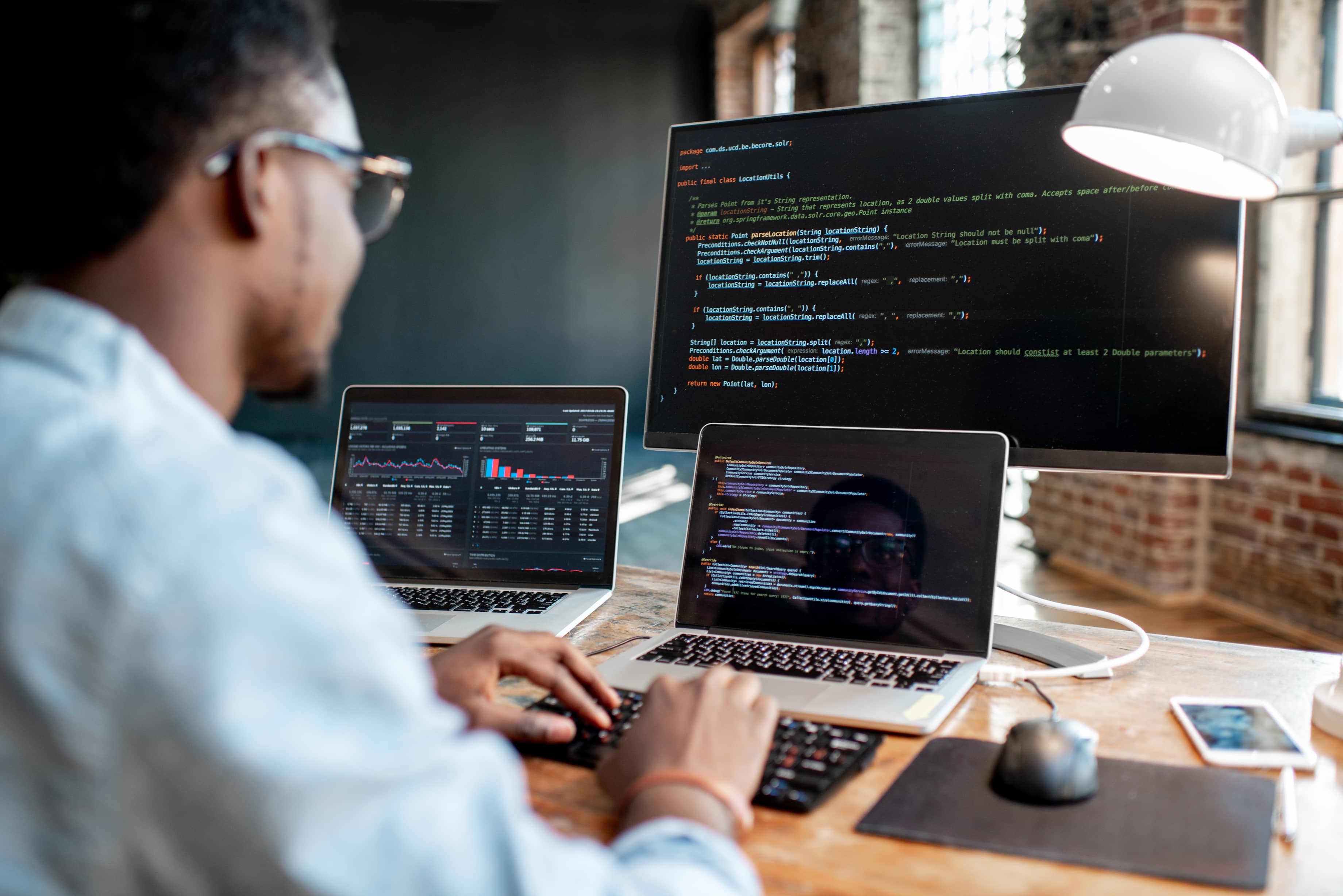 A tech professional working in code across three monitors.