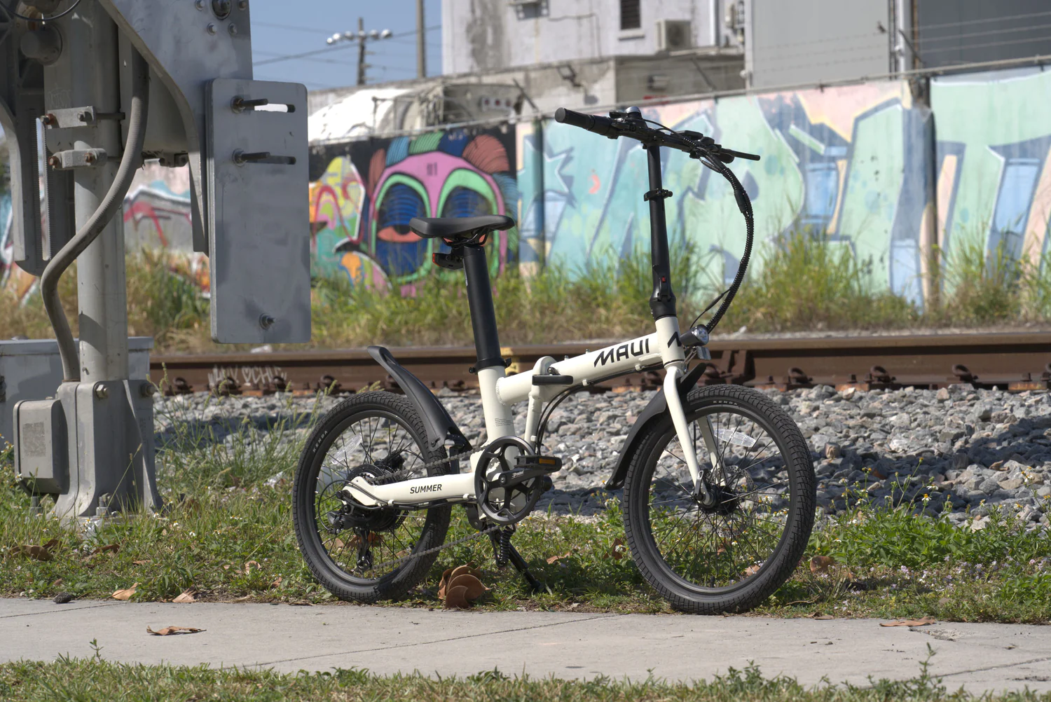 White Maui Summer folding electric bike parked near graffiti wall