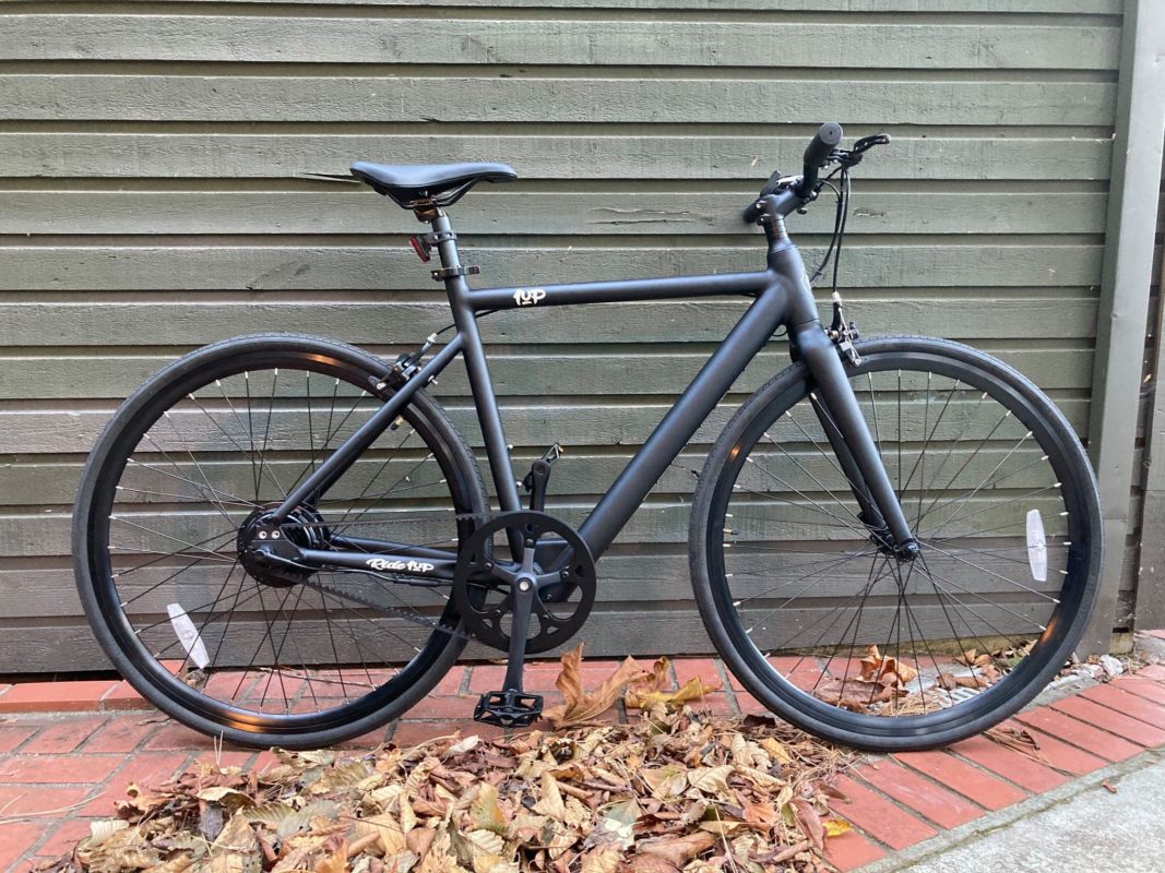 Matte black bicycle with thin tires parked on brick path with autumn leaves