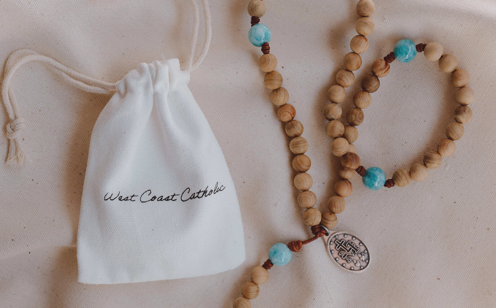 Wooden rosary with turquoise beads and religious medal beside white drawstring bag