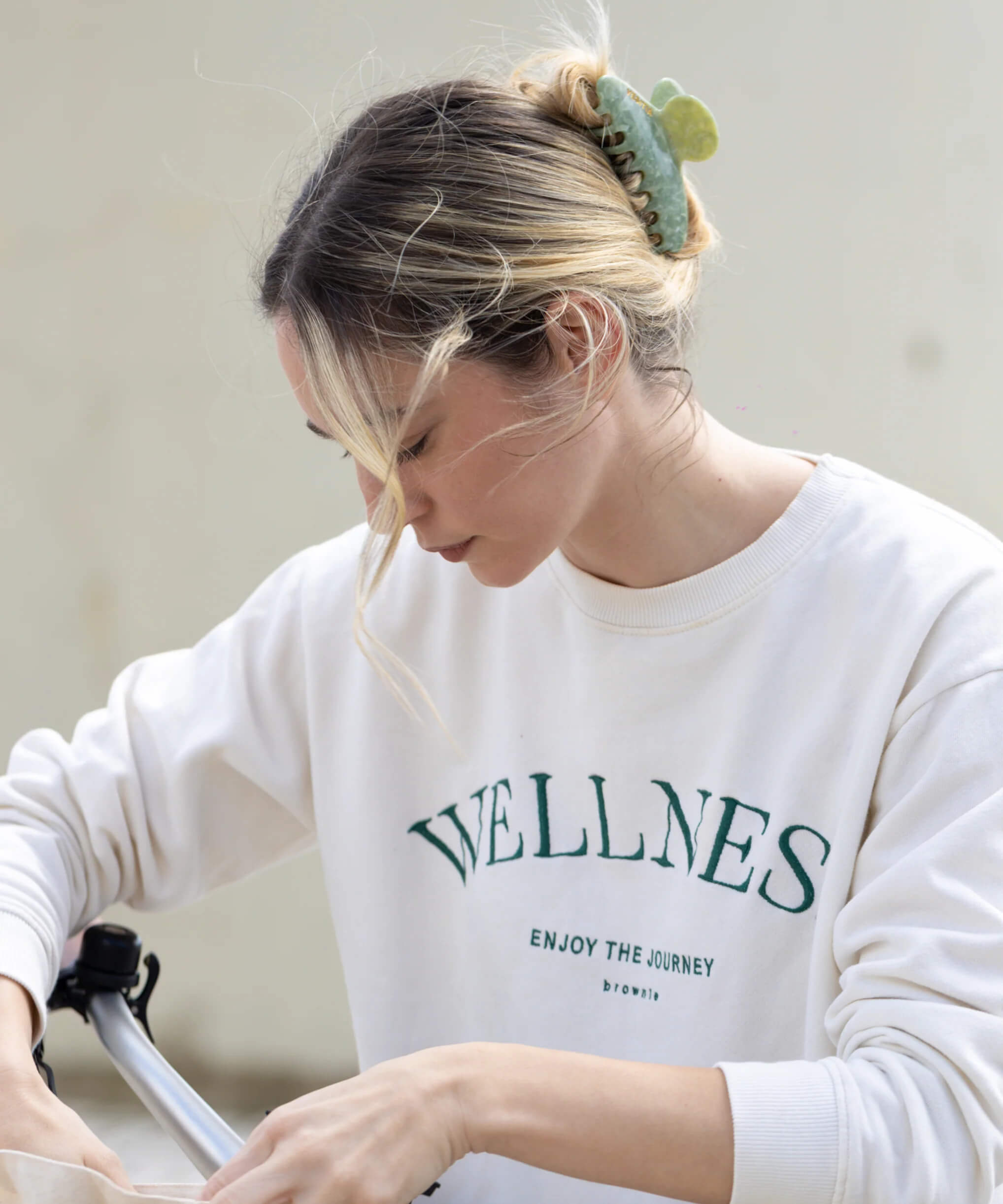 Woman in white wellness sweatshirt with hair clip looking down